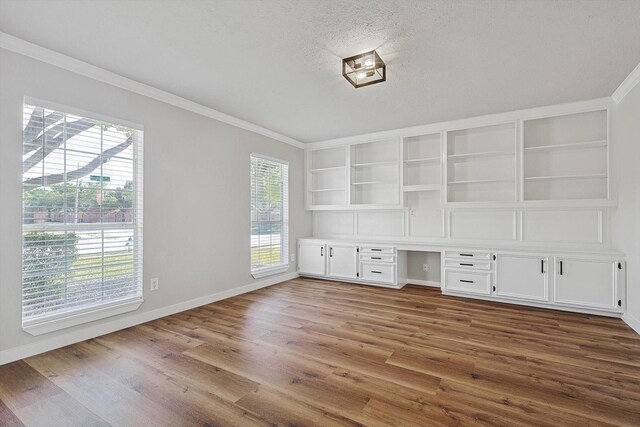 unfurnished office featuring a healthy amount of sunlight, wood-type flooring, and built in desk