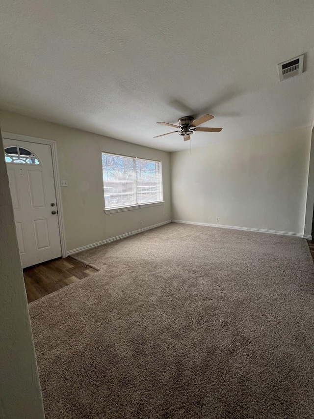 interior space featuring baseboards, visible vents, dark carpet, and a textured ceiling