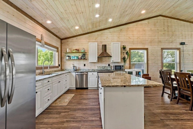 kitchen featuring lofted ceiling, wall chimney range hood, stainless steel appliances, light stone counters, and a kitchen island
