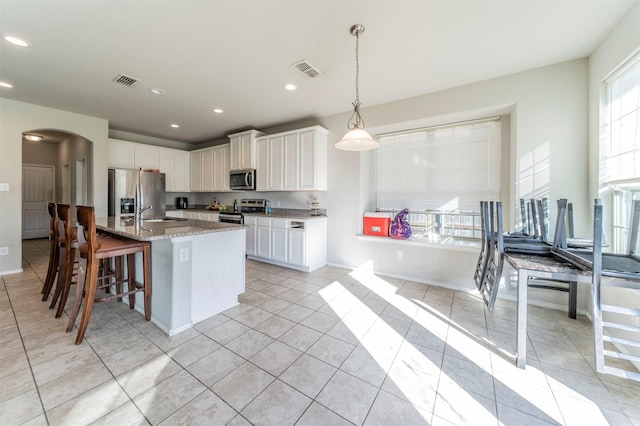 kitchen with stainless steel appliances, light tile patterned floors, pendant lighting, a center island with sink, and white cabinets