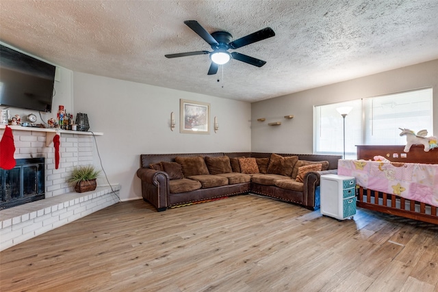 living room with a fireplace, a textured ceiling, light hardwood / wood-style flooring, and ceiling fan