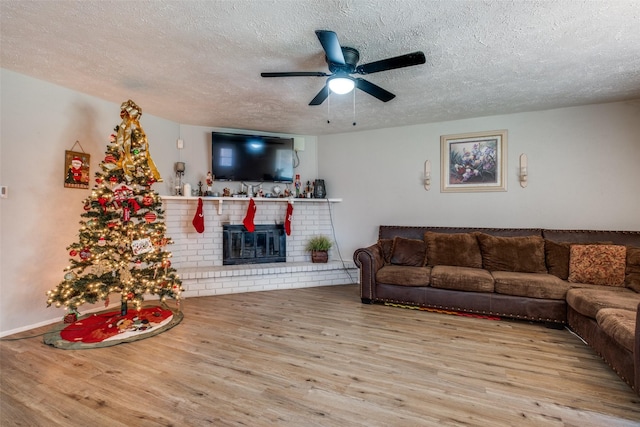 living room with ceiling fan, a fireplace, light hardwood / wood-style floors, and a textured ceiling