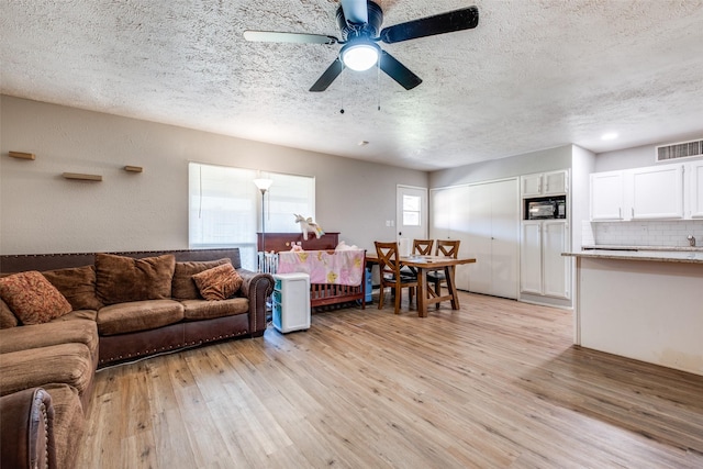 living room featuring ceiling fan, a textured ceiling, and light wood-type flooring