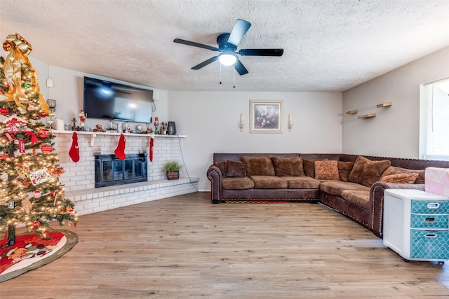 living room featuring a fireplace, a textured ceiling, light hardwood / wood-style flooring, and ceiling fan