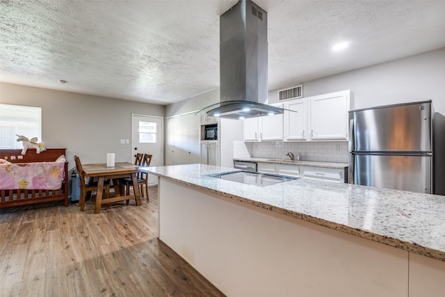 kitchen with stainless steel fridge, light stone counters, island range hood, electric stovetop, and white cabinets