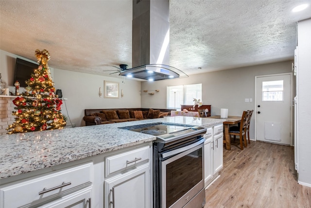 kitchen with island exhaust hood, light stone counters, stainless steel electric stove, white cabinetry, and plenty of natural light