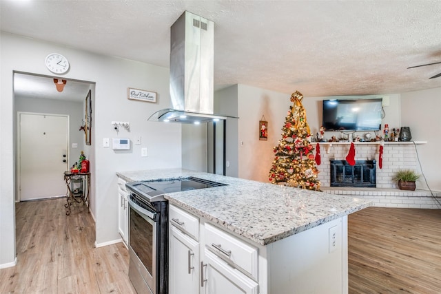 kitchen with light stone counters, stainless steel range with electric cooktop, island exhaust hood, white cabinets, and light wood-type flooring