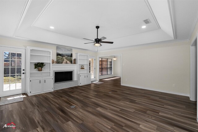 unfurnished living room with built in shelves, ceiling fan, a brick fireplace, a raised ceiling, and dark hardwood / wood-style floors