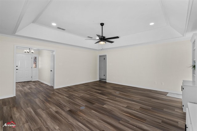 unfurnished living room featuring ceiling fan with notable chandelier, a tray ceiling, crown molding, and dark wood-type flooring