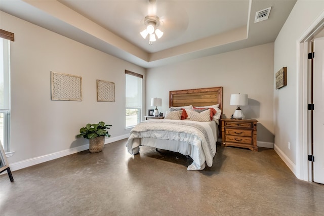 bedroom with concrete floors, a tray ceiling, and ceiling fan