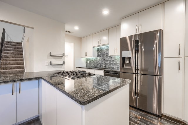 kitchen with white cabinetry, sink, backsplash, dark stone counters, and stainless steel appliances