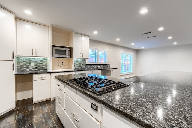 kitchen with white cabinetry, stainless steel microwave, black gas stovetop, and dark stone counters