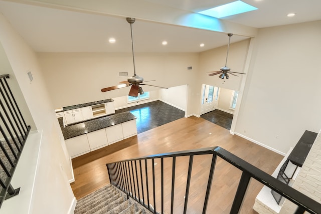 staircase featuring ceiling fan, high vaulted ceiling, a skylight, and hardwood / wood-style floors