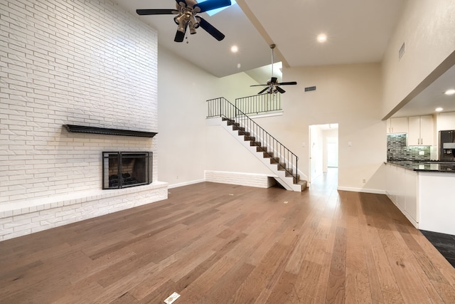 unfurnished living room with hardwood / wood-style flooring, a towering ceiling, a fireplace, and ceiling fan