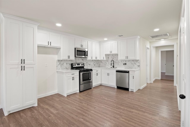 kitchen with sink, light wood-type flooring, appliances with stainless steel finishes, white cabinets, and backsplash