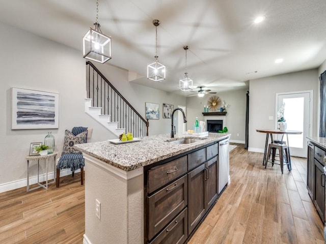 kitchen featuring sink, light hardwood / wood-style flooring, hanging light fixtures, light stone counters, and stainless steel dishwasher