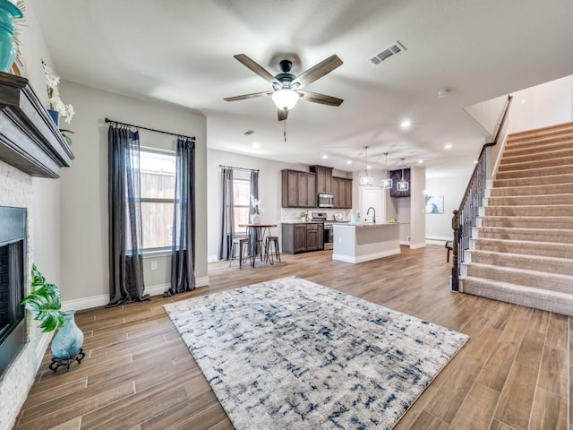 living room with light hardwood / wood-style flooring, sink, a fireplace, and ceiling fan