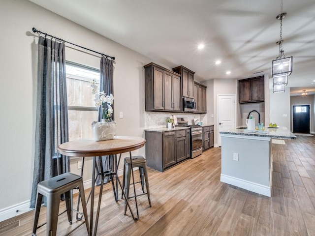 kitchen featuring light stone countertops, appliances with stainless steel finishes, light wood-type flooring, and dark brown cabinetry