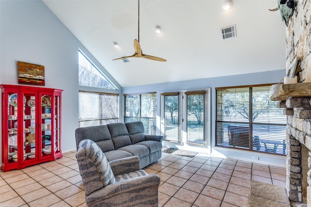 tiled living room featuring a stone fireplace, ceiling fan, and high vaulted ceiling