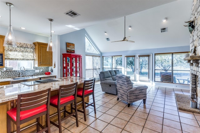 kitchen featuring decorative backsplash, light stone counters, a breakfast bar, high vaulted ceiling, and light tile patterned flooring