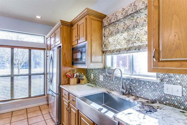 kitchen featuring light stone countertops, tasteful backsplash, black microwave, sink, and light tile patterned floors