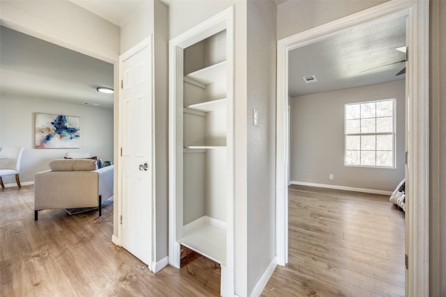 hallway with built in shelves, light hardwood / wood-style floors, and a textured ceiling