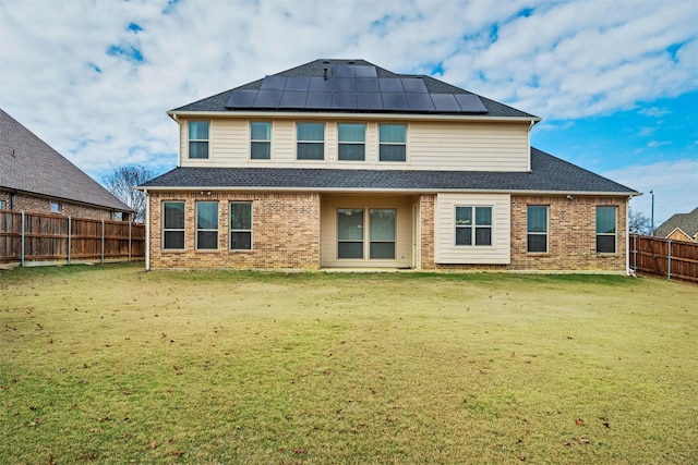 rear view of house with a fenced backyard, roof mounted solar panels, a lawn, and brick siding