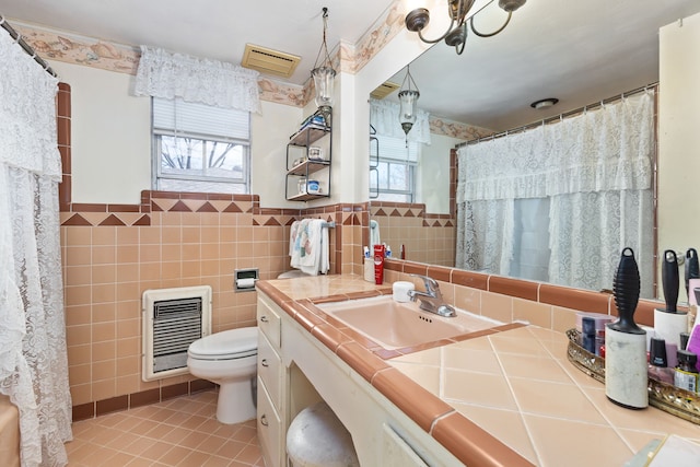 bathroom with tile patterned floors, heating unit, toilet, vanity, and tile walls