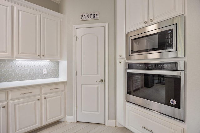 kitchen with appliances with stainless steel finishes, backsplash, light hardwood / wood-style flooring, and white cabinetry