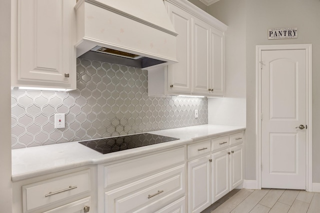 kitchen with black electric cooktop, white cabinetry, custom range hood, and decorative backsplash