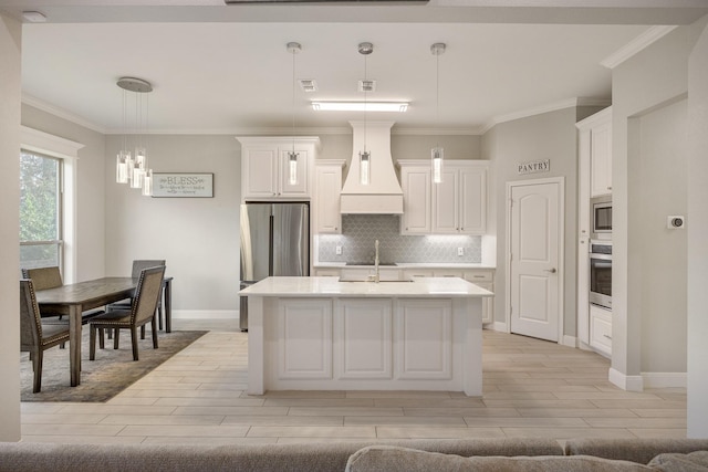 kitchen featuring backsplash, custom range hood, stainless steel appliances, decorative light fixtures, and a center island with sink