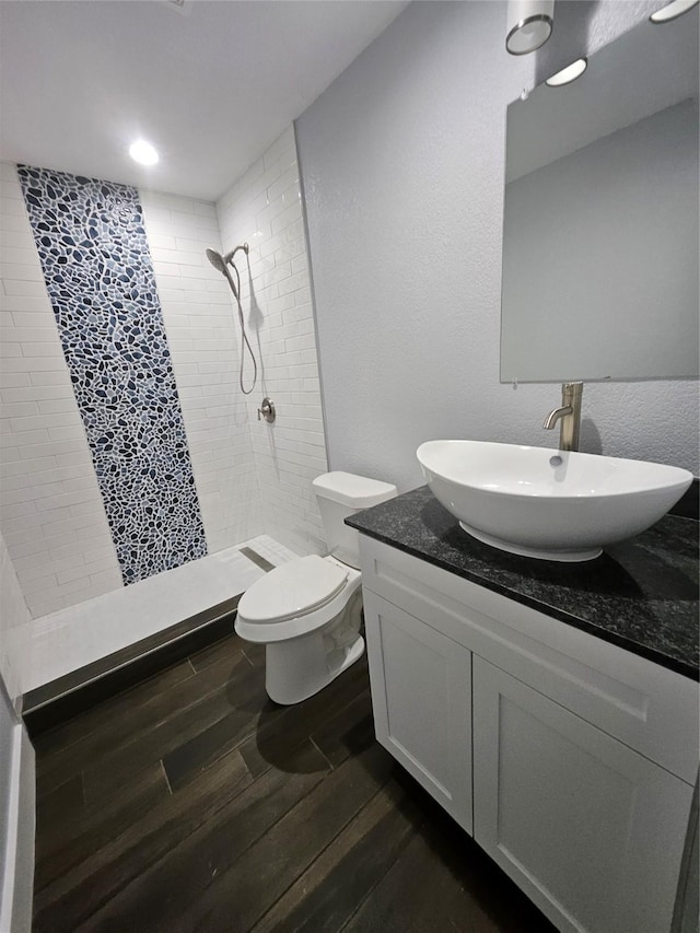 bathroom with hardwood / wood-style flooring, vanity, toilet, and a tile shower