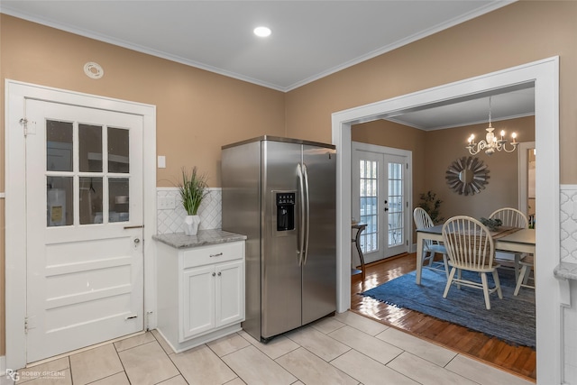 kitchen with stainless steel refrigerator with ice dispenser, french doors, light tile patterned floors, decorative light fixtures, and white cabinetry