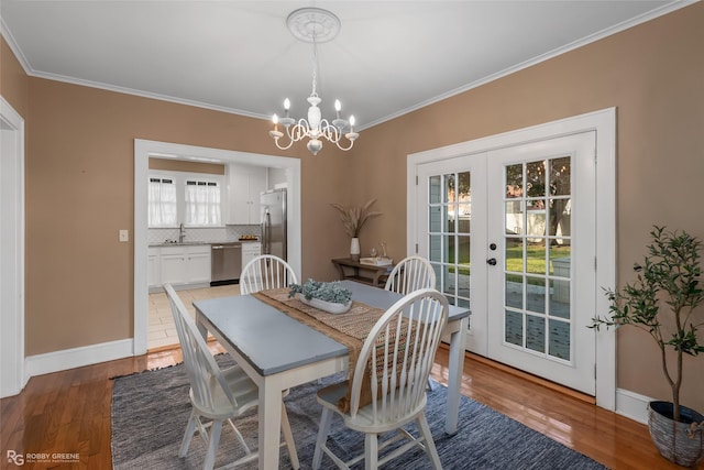 dining room with sink, light wood-type flooring, ornamental molding, an inviting chandelier, and french doors