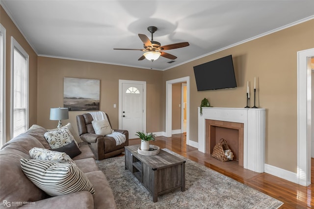 living room with a fireplace, crown molding, wood-type flooring, and ceiling fan