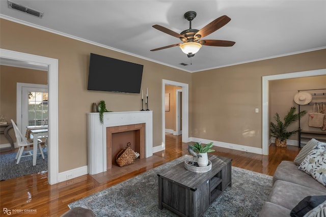 living room featuring ceiling fan, ornamental molding, dark hardwood / wood-style flooring, and a tile fireplace