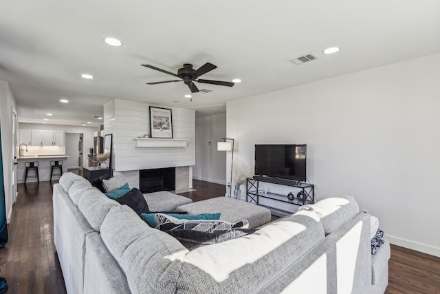 living room featuring ceiling fan, a large fireplace, sink, and dark wood-type flooring