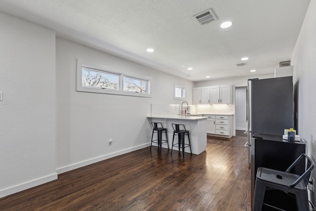 kitchen with sink, a breakfast bar area, white cabinetry, dark hardwood / wood-style floors, and kitchen peninsula