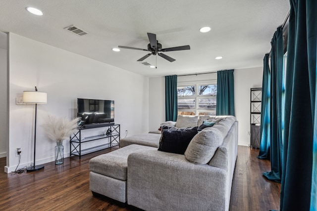 living room featuring ceiling fan, dark wood-type flooring, and a textured ceiling