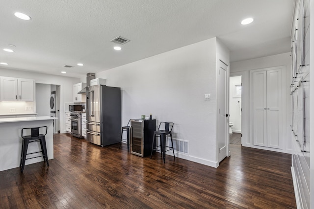 kitchen featuring stacked washing maching and dryer, high quality appliances, white cabinetry, dark wood-type flooring, and wall chimney range hood