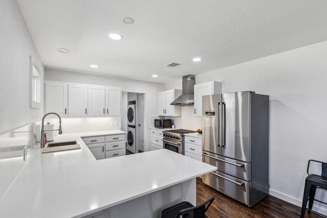 kitchen featuring sink, wall chimney range hood, kitchen peninsula, stacked washer / dryer, and high end appliances