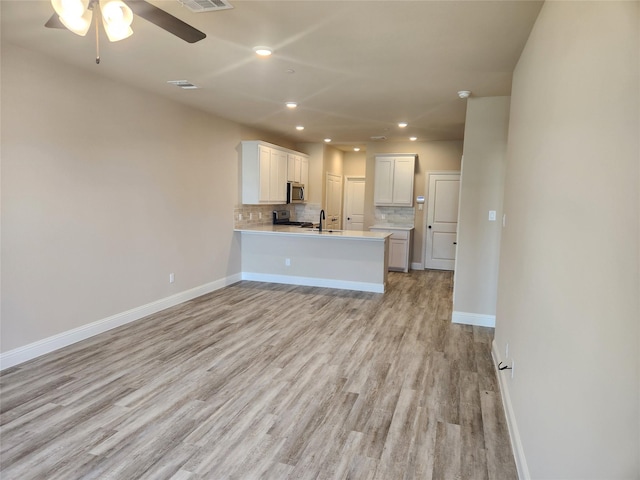 kitchen featuring kitchen peninsula, light hardwood / wood-style flooring, decorative backsplash, appliances with stainless steel finishes, and white cabinetry