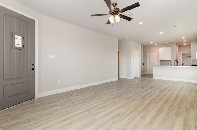 unfurnished living room featuring light wood-type flooring, ceiling fan, and sink