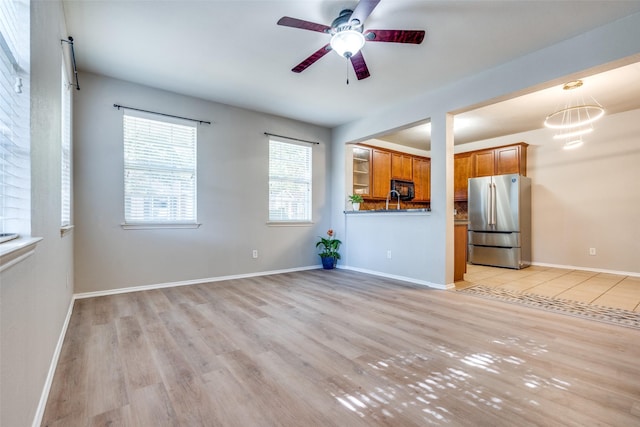 unfurnished living room featuring ceiling fan with notable chandelier and light hardwood / wood-style flooring