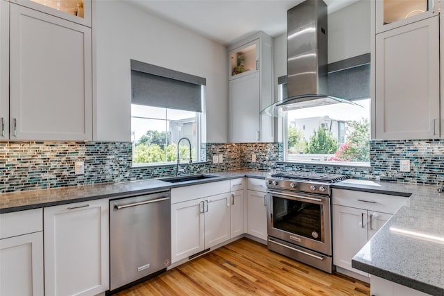 kitchen with appliances with stainless steel finishes, tasteful backsplash, wall chimney exhaust hood, sink, and white cabinetry