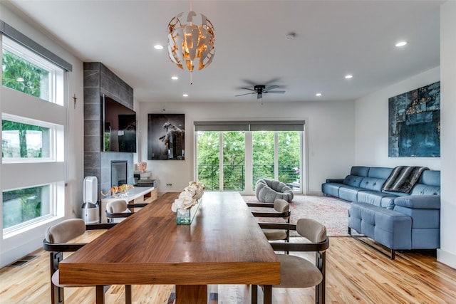 dining area featuring ceiling fan with notable chandelier, light wood-type flooring, and a tiled fireplace