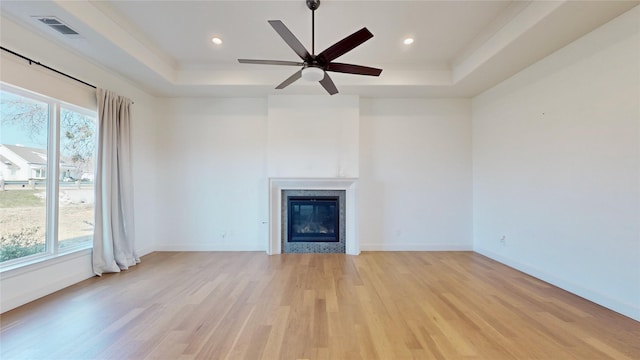 unfurnished living room with a tray ceiling, ceiling fan, and light wood-type flooring