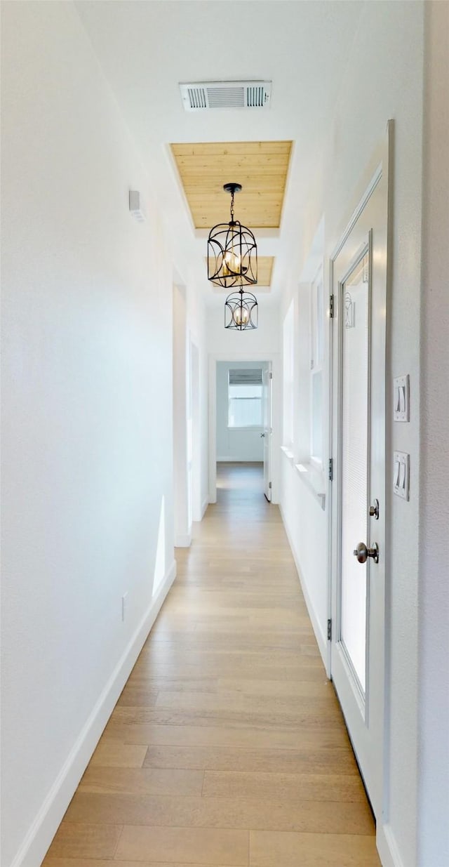 hallway with a raised ceiling, light wood-type flooring, wood ceiling, and a chandelier