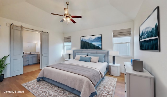 bedroom with ceiling fan, ensuite bathroom, vaulted ceiling, a barn door, and light wood-type flooring