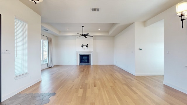 unfurnished living room with ceiling fan, light wood-type flooring, a fireplace, and a tray ceiling